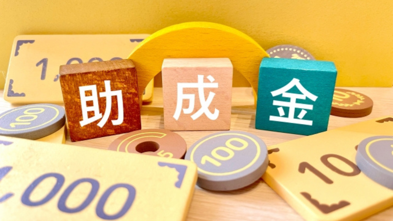 補助金等の情報お知らせ記事に使用した助成金と書かれたサイコロとおもちゃのお金が並んだ画像